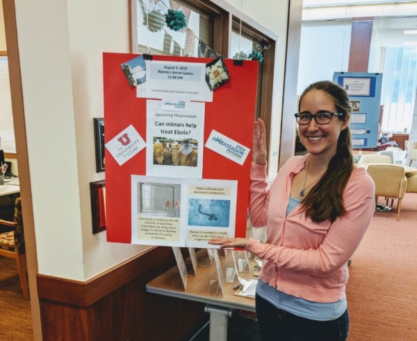 Ambassador Sarah Apple poses beside a poster for her talk at Riverton Senior Center.