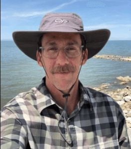 dave parrot wearing a hat while standing in front of a body of water