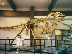 Young Patricia Girardi standing in front of a dinosaur skeleton